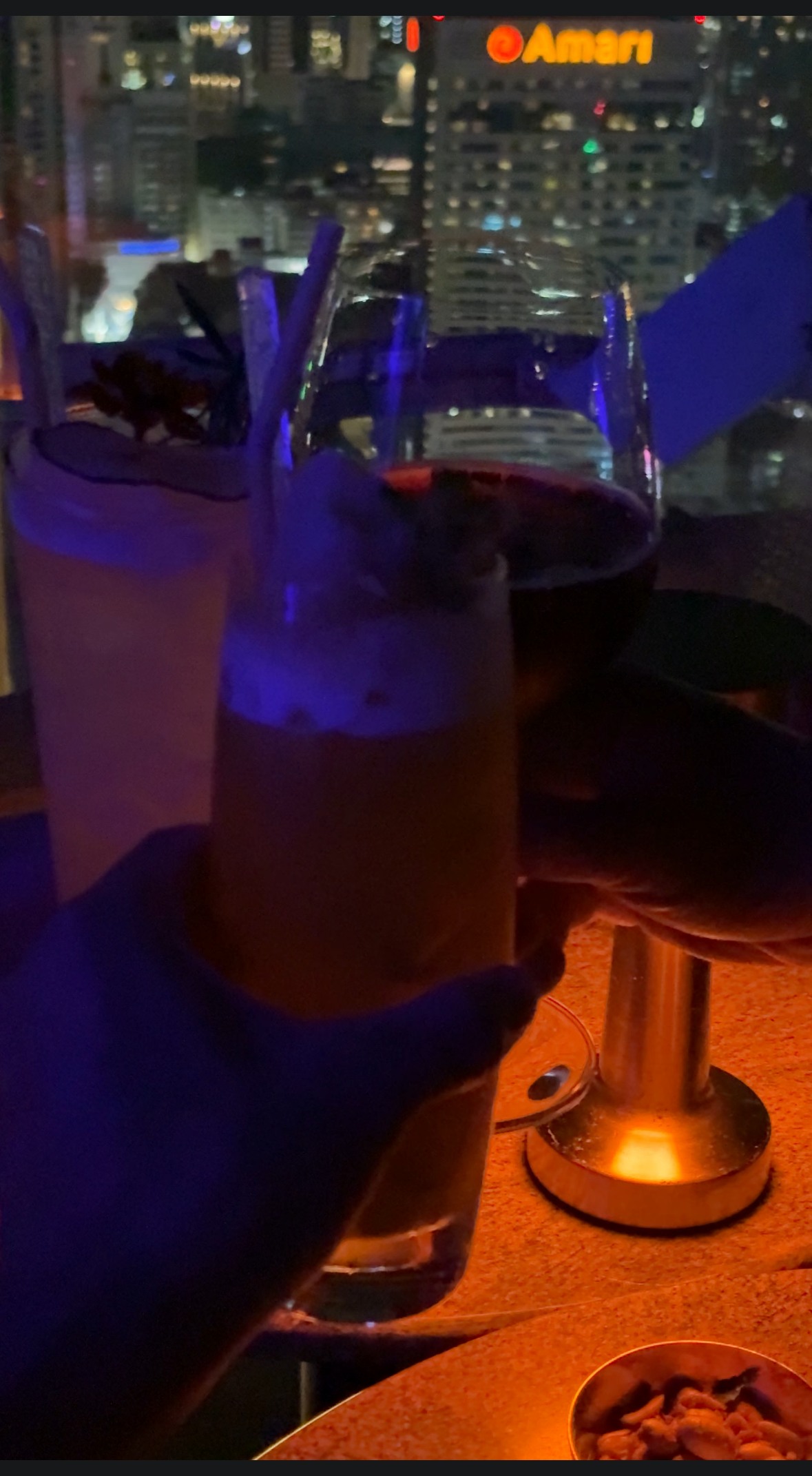 マンゴー・パイナップルカクテルで乾杯する様子と夜景の中の「Amari」ホテル看板